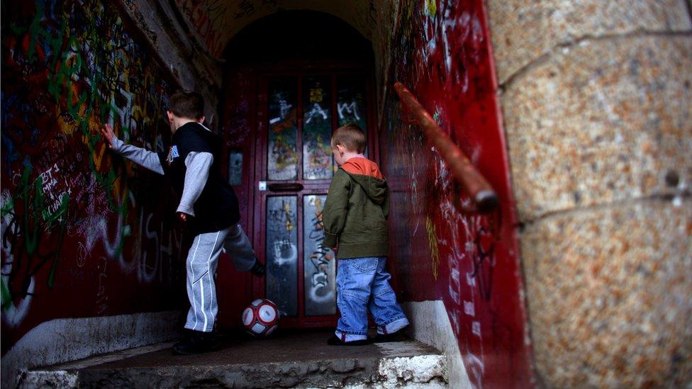 Two young boys play football in the doorway of a run-down building