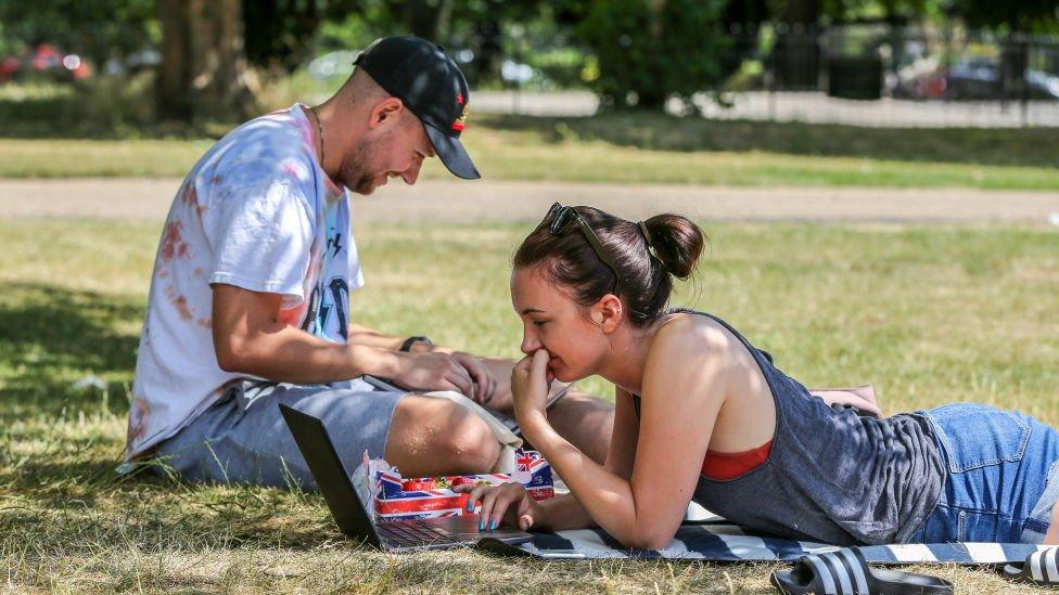 A couple working on their laptops under the shade on a hot and sunny day London