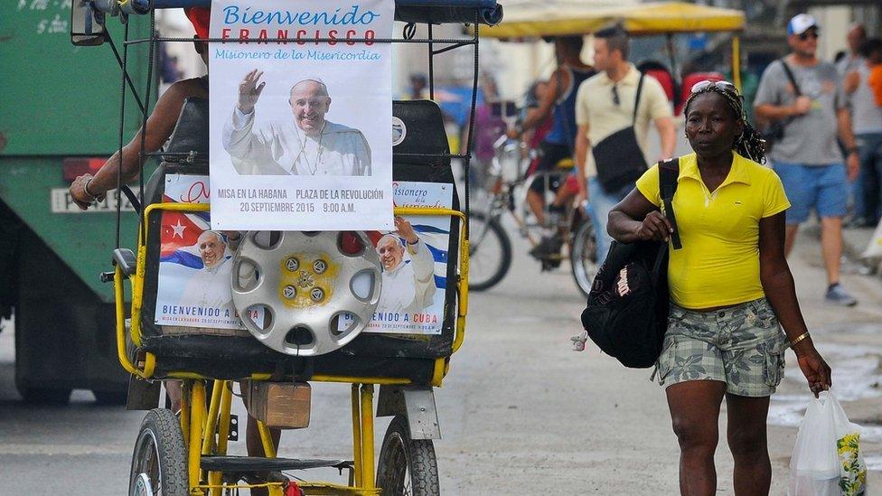 A cycle rickshaw decorated with a poster depicting Pope Francis drives along a street of Havana.