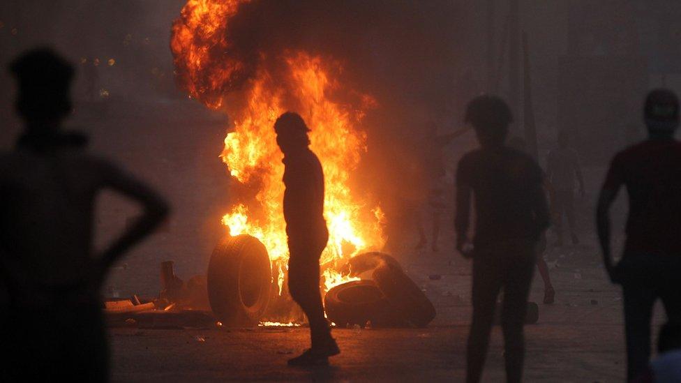 A man stands in front of a burning tyre