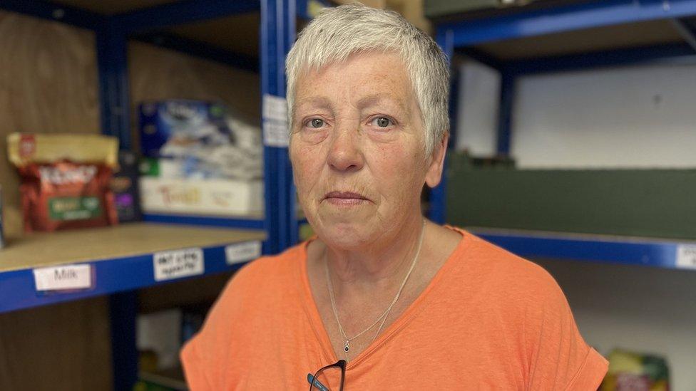 A woman in an orange top next to empty food shelves