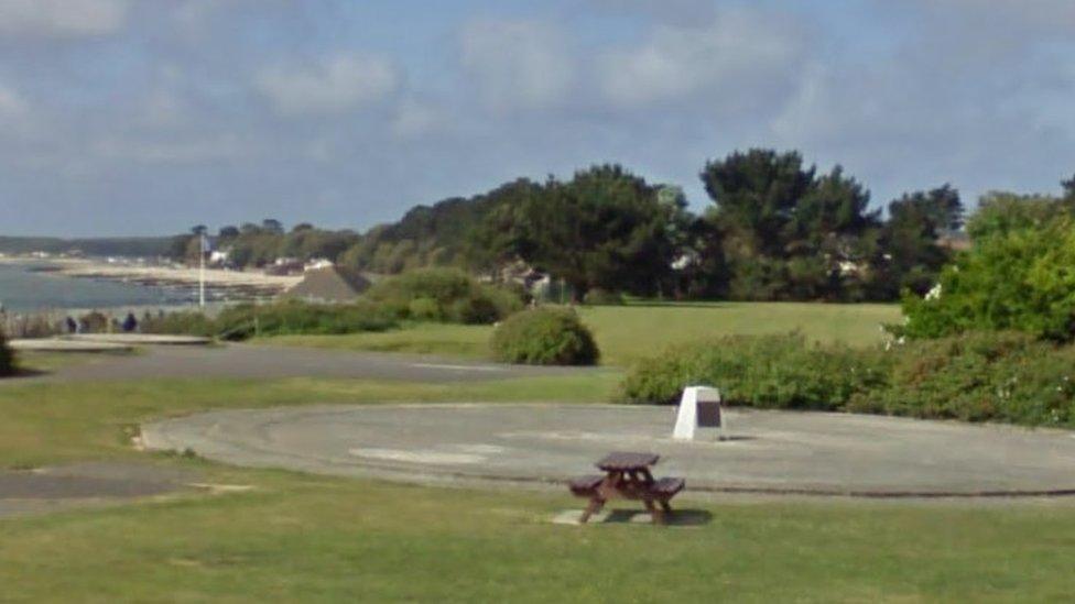 Circular concrete base in the middle of a park with the sea in the background