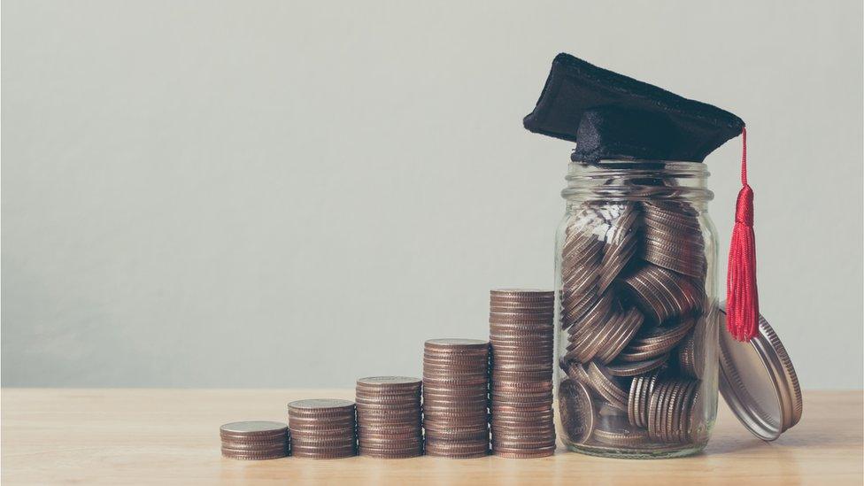 Different sized piles of coins in a row, next to a jar with a mortar board on it