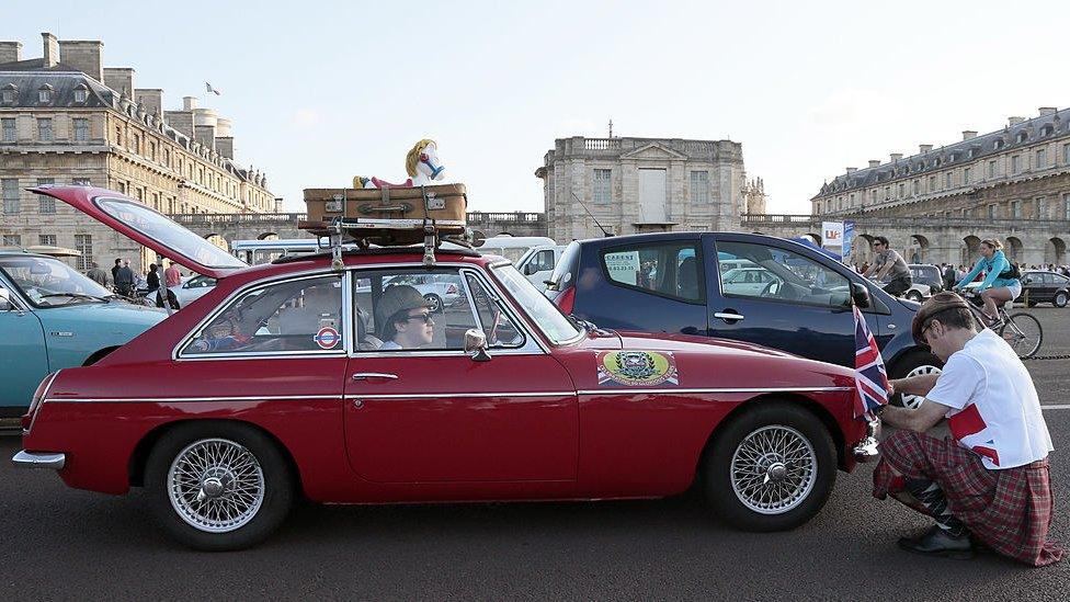 A man puts an Union Jack flag on his MG next to the Chateau de Vincennes, outside Paris