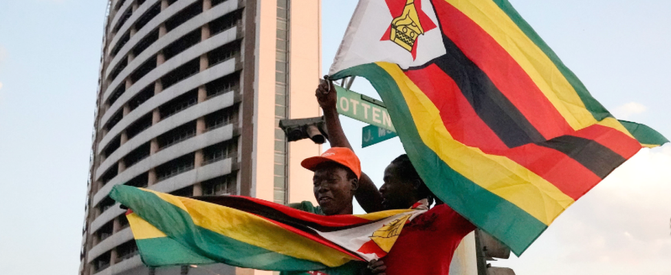 People holding Zimbabwean flags celebrate in the street after the resignation of Robert Mugabe as president on 21 November 2017 in Harare, Zimbabwe