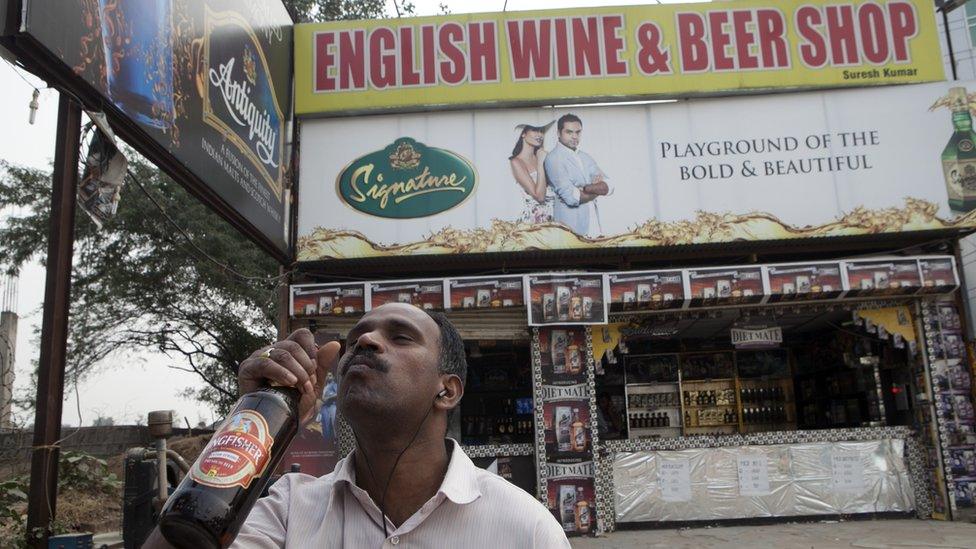 A man takes a swig of Kingfisher beer outside a liquor store