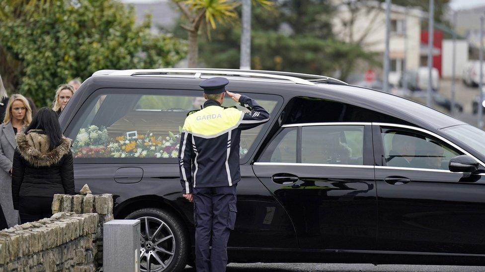 A police officer salutes a hearse carrying James O'Flaherty