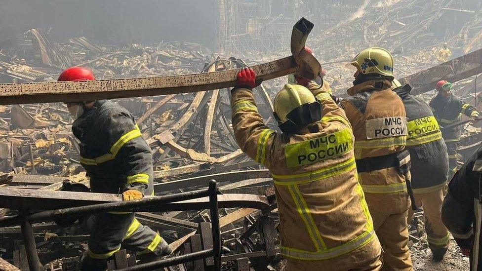 Russian emergency service workers lift a metal bar and search through rubble