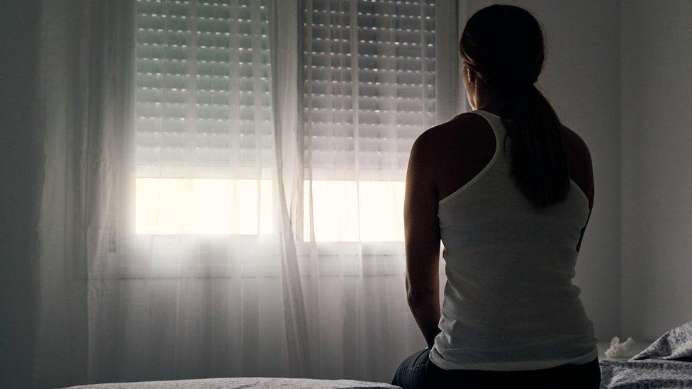 A woman sits alone opposite a window