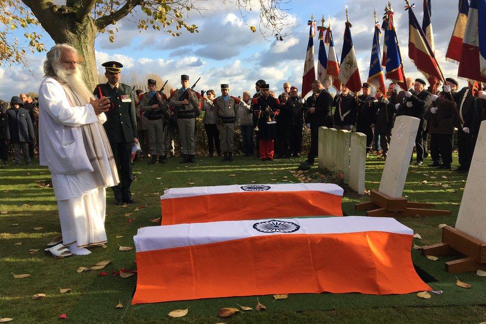 A Hindu priest chants in front of two coffins draped with the Indian flag