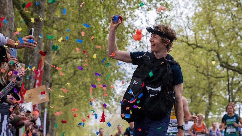 George Scholey running along the course carrying a Rubik's Cube, which he is showing to the crowd