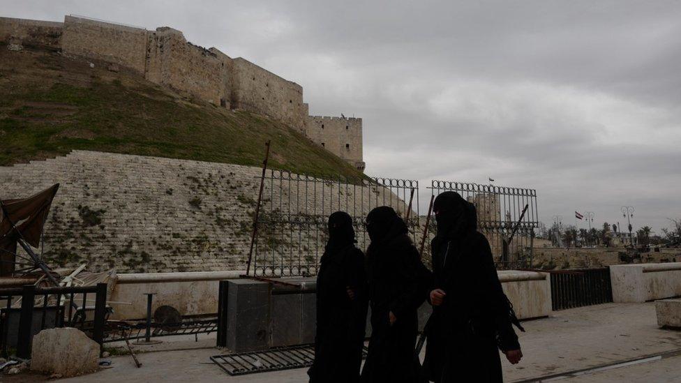 Three women dressed in the niqab walk in front of the citadel in Aleppo