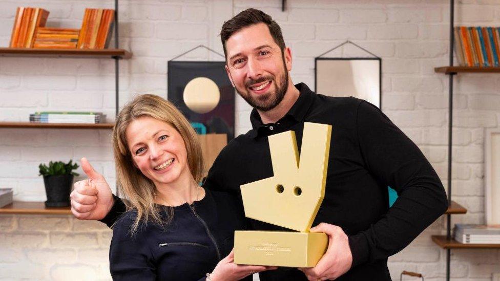 Man with short dark beard and woman with long fair hair hold an award shaped like the Deliveroo kangaroo