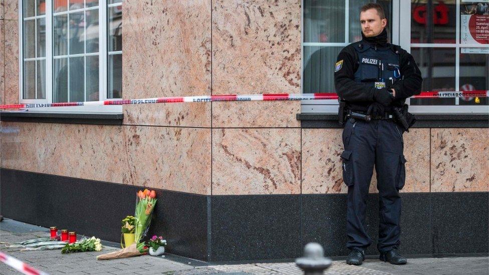 A policeman stands next to some flowers left at the scene of the shooting in Hanau