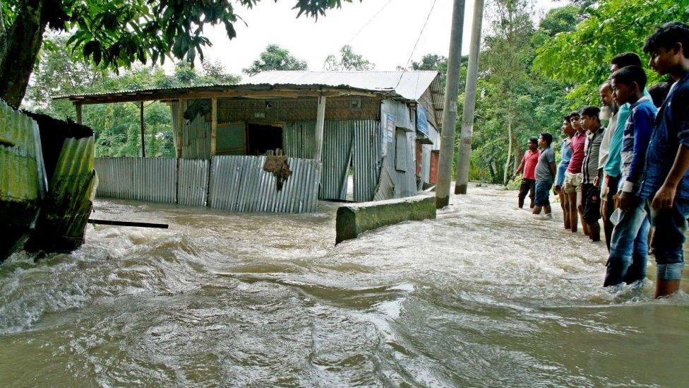 Bystanders watch floodwaters rage near a house in Kurigram, northern Bangladesh.