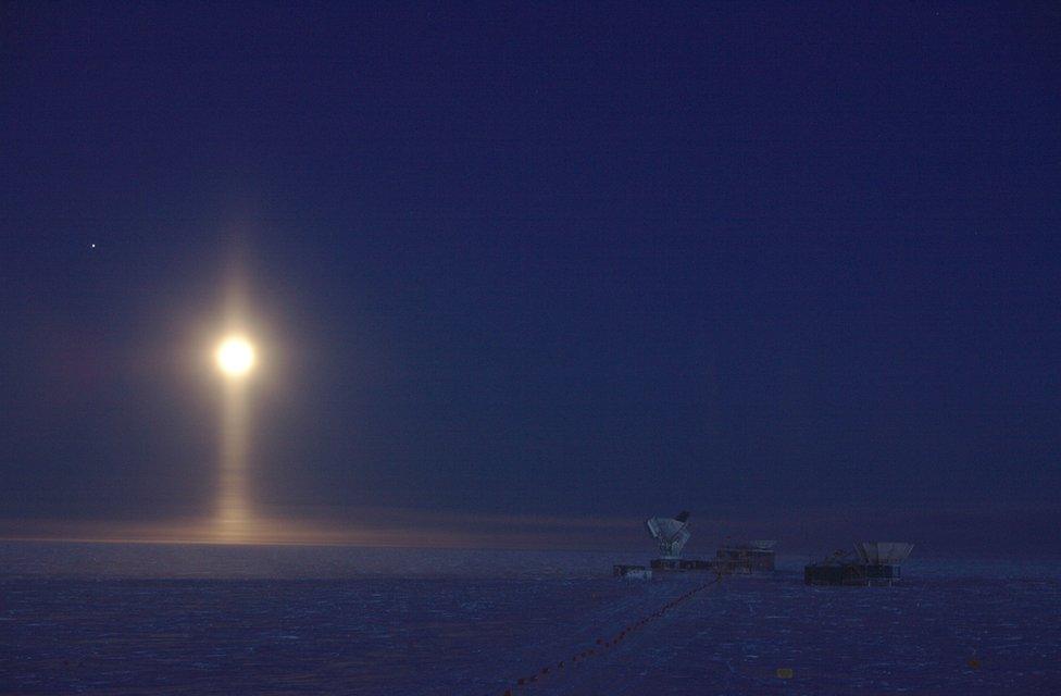 Moon in dark sky with a pillar of light below