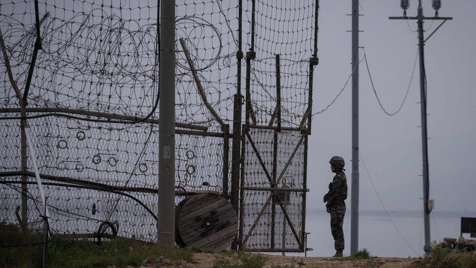 A soldier stands guard at an opening to the fence of the Demilitarized Zone (DMZ) during maintenance, on Gyodong, a tiny outlying island near to the west of Seoul, on 9 May 2017