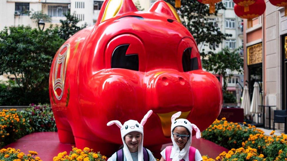 Children in animal hats pose in front of a pig giant pig installation ahead of the Lunar New Year in Hong Kong