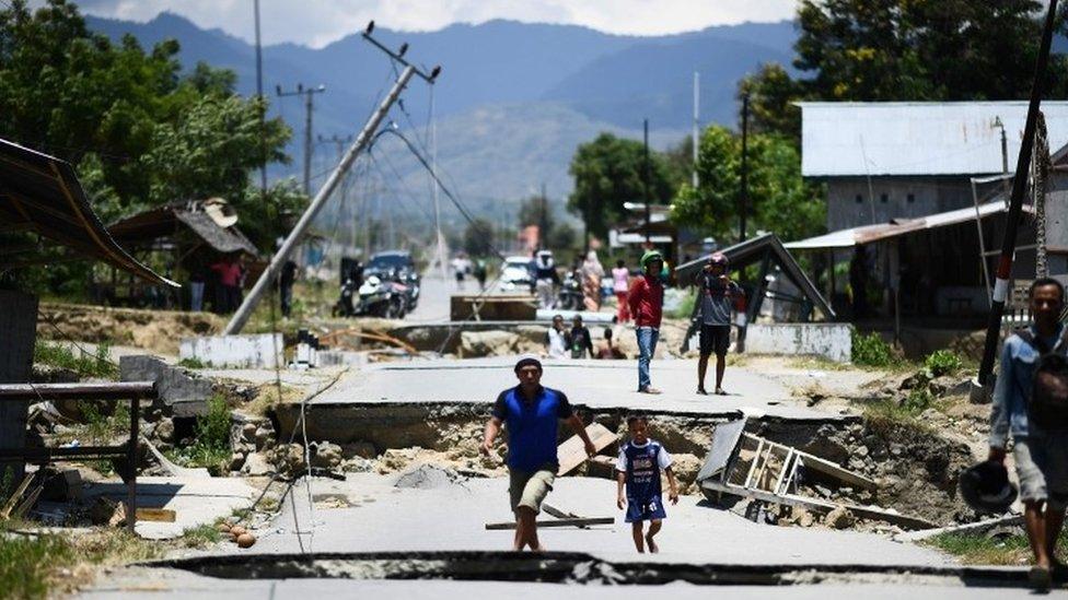 Survivors walk on a damaged street outside Palu in Indonesia's Central Sulawesi on October 2, 2018