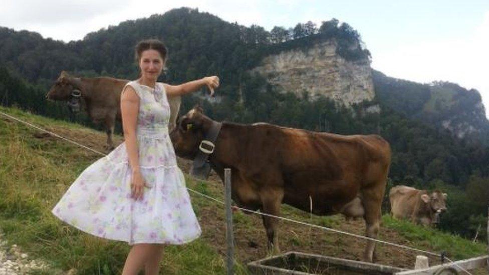 Nancy giving a thumbs down to cows wearing bells in a fenced-in field