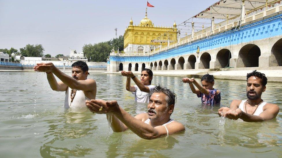 men-and-women-stand-in-water-at-temple-offering-hands-full-of-water-upwards