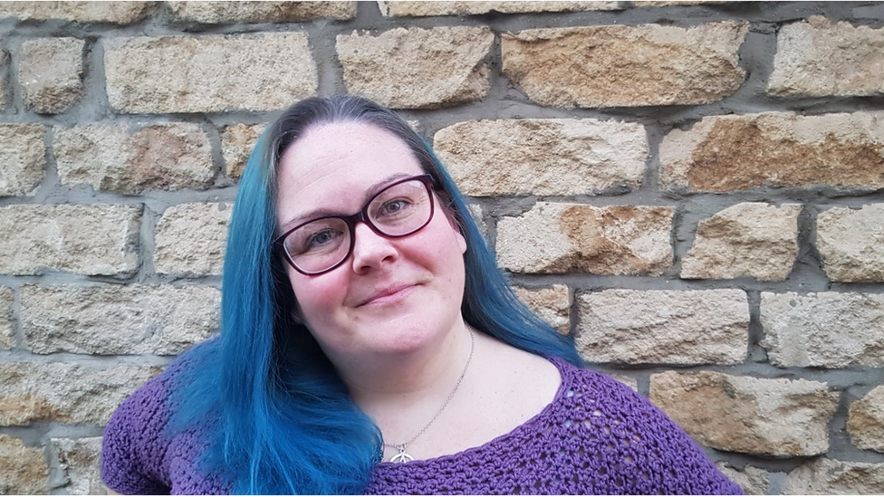 Pam Paterson smiling into the camera. She has blue hair and is wearing glasses.