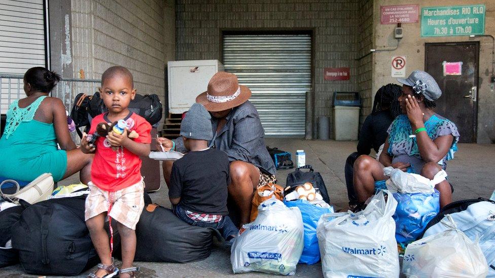 A group of Haitian asylum seekers sit with shopping bags outside the Olympic Stadium, which is being used for temporary housing for asylum seekers, in Montreal, Quebec