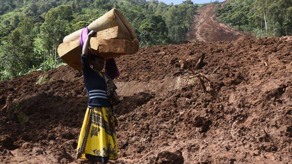 A woman carries a rolled-up mattress at a landslide site in Shisakali village of Bududa district, eastern Uganda,