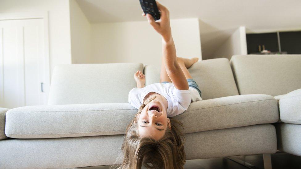 girl-upside-on-sofa-pointing-tv-remote.