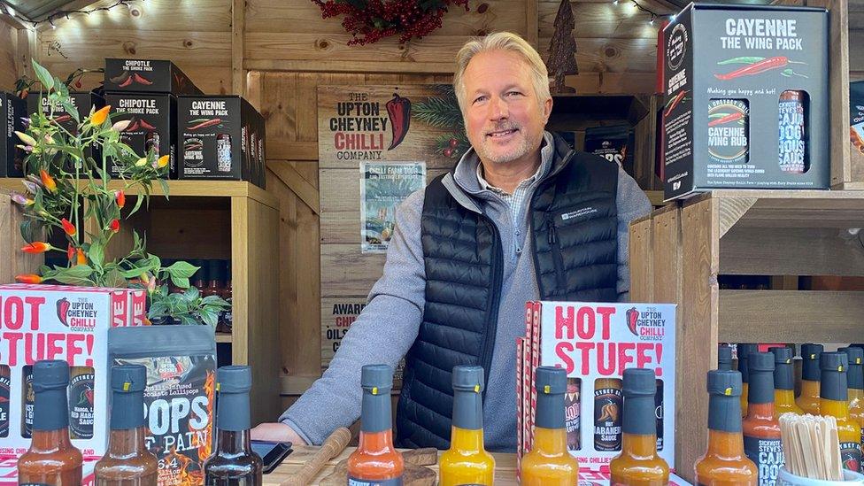 Man wearing blue gilet smiling at camera from a wooden stall