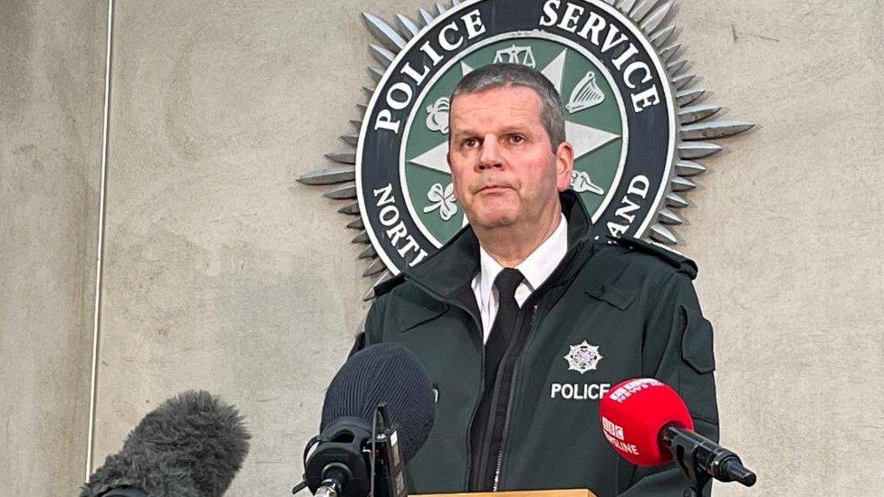 PSNI Assistant Chief Constable Chris Todd speaks to members of the the media. The force's logo can be seen on a wall behind him.