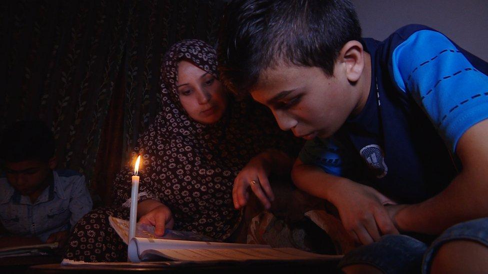 Mother and son read by candlelight in an apartment in Gaza City