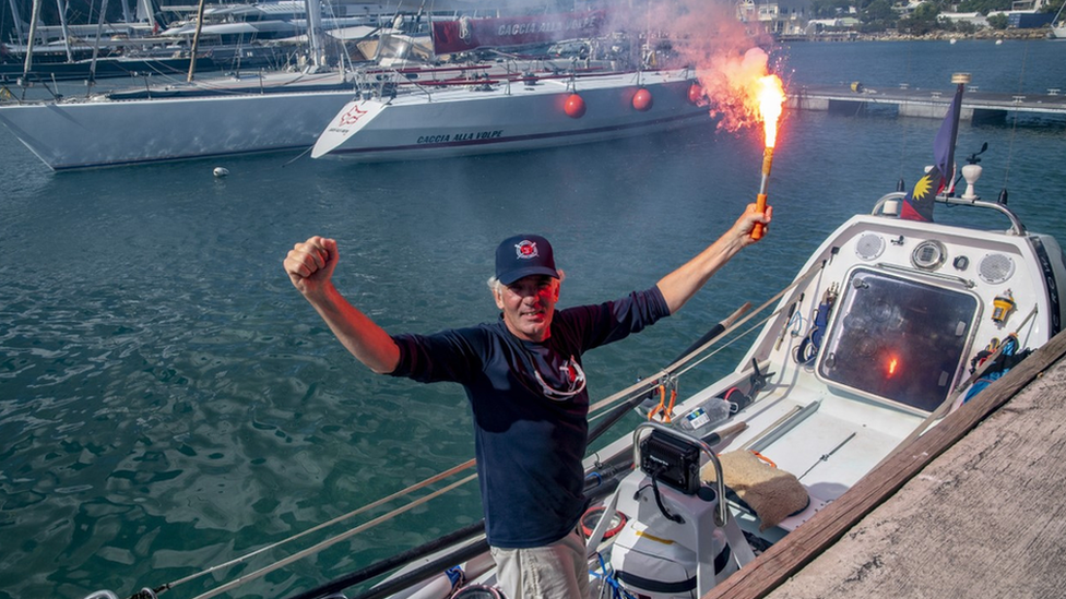 Andrew Osborne with his arms up holding a flare on his boat