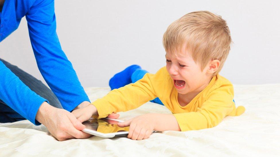 crying boy holding tablet