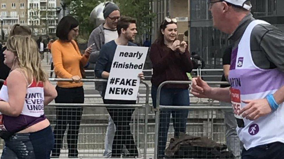 Photo of a spectator holding up a sign which says 'nearly finished #FAKENEWS'