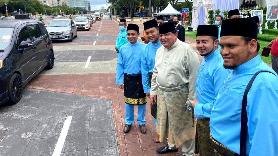 Queue of cars passing by wedding guests.