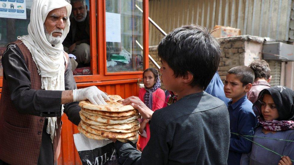 File photo showing an Afghan boy receives free bread outside a bakery in Kabul (3 May 2020)