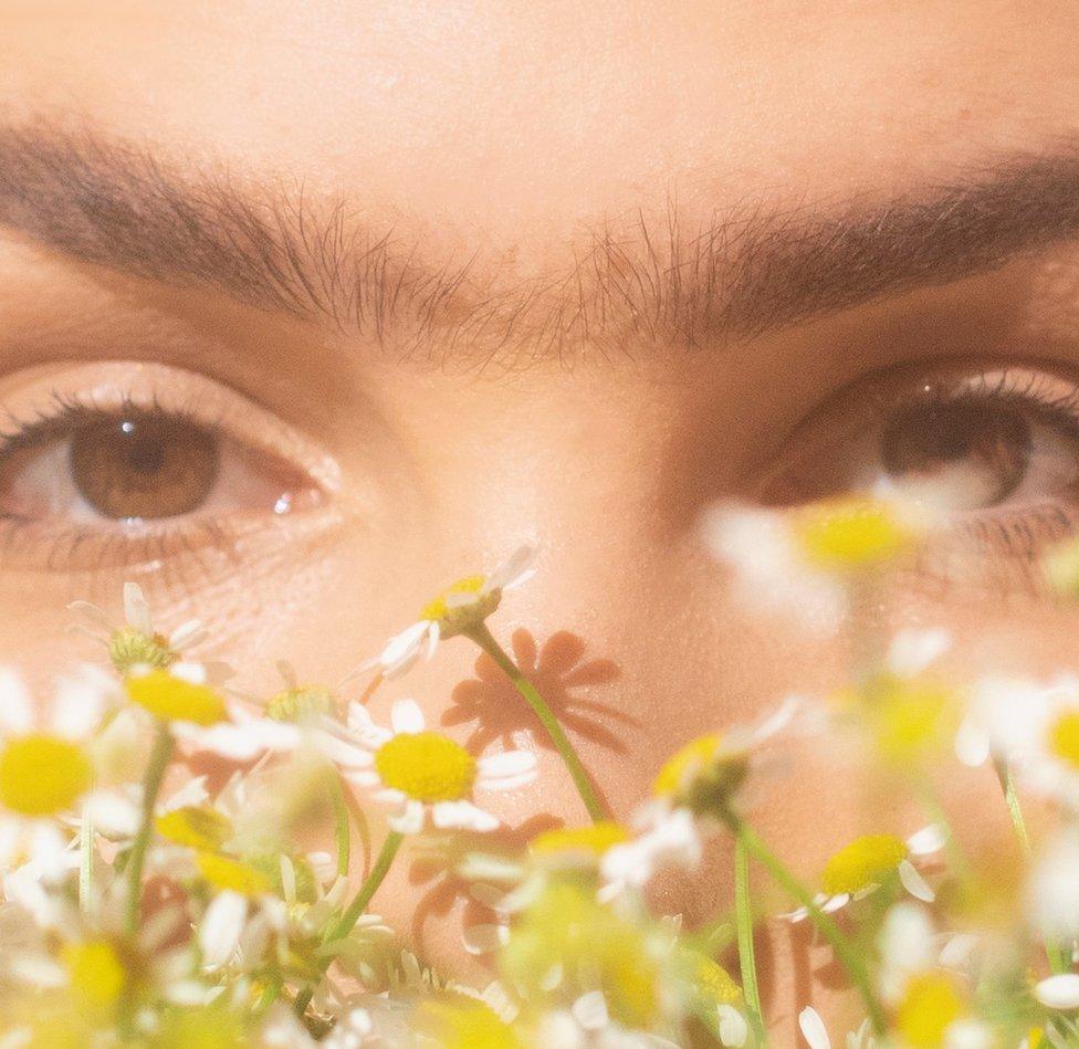 A close-up shot of a young woman with a monobrow (hair between the eyebrows which gives the impression of a single unbroken brow)