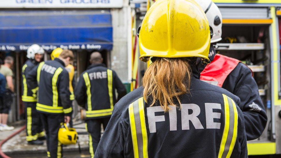 File photo showing an anonymous female firefighter with male colleagues putting away kit in the background