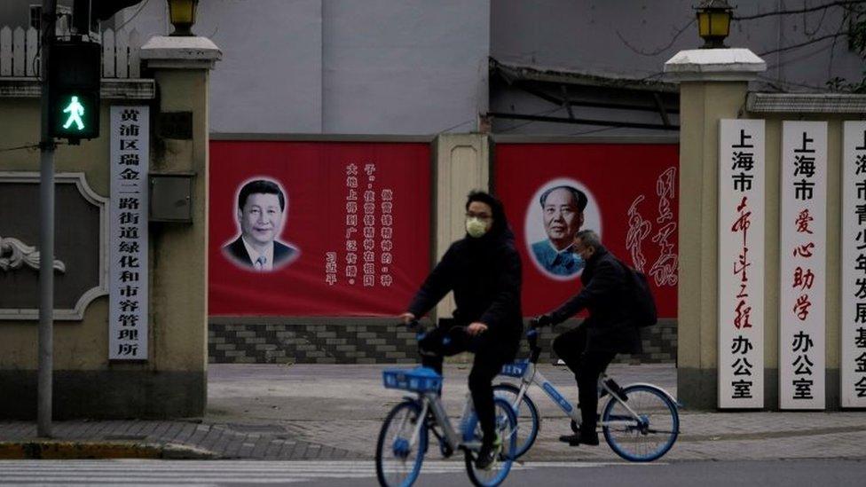 People wearing masks pass by portraits of Chinese President Xi Jinping and late Chinese chairman Mao Zedong