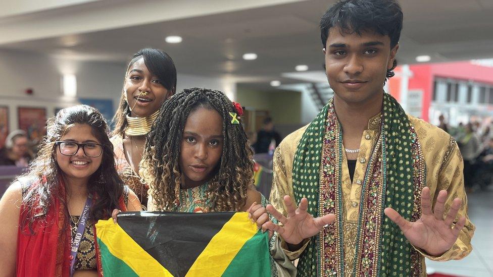 four students of different heritages stand on a catwalk in national dress