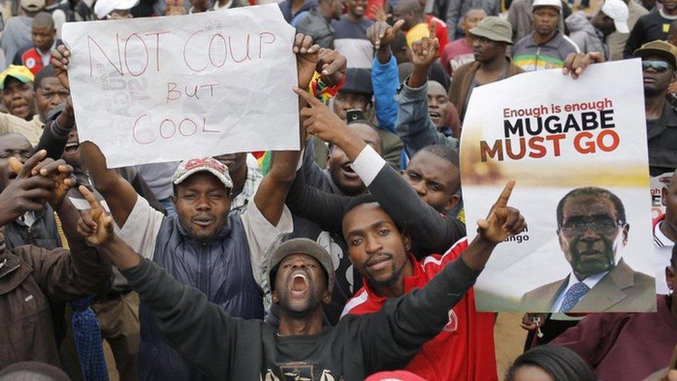 people holding signs reading "not coup but cool" and "Mugabe must go" in the midst of a sea of people