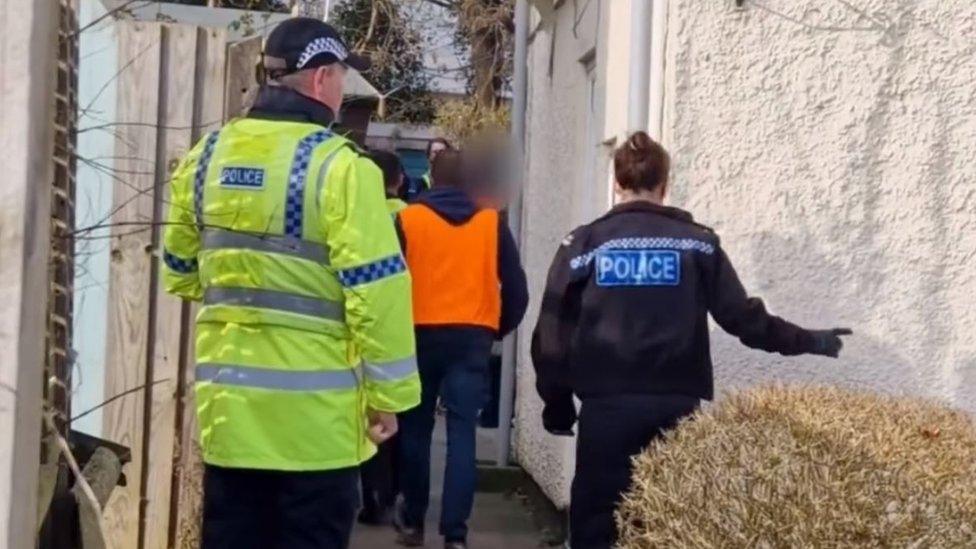 Police officers outside a home from which they are seizing drugs or illegal substances