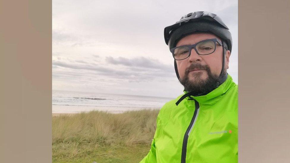 Man with beard and glasses wearing a cycle helmet and yellow hi-viz