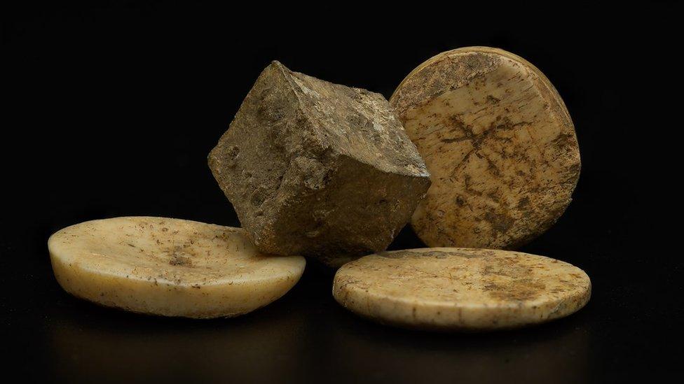 picture shows close up of a cube shape and several flat discs that look like counters, dirty and worn away