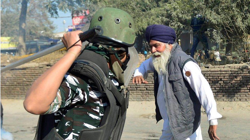 A police officer raises his baton to hit a farmer