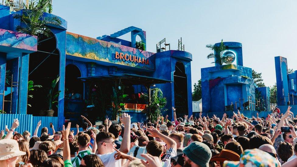 Festival-goers dancing in the sun next to a stage