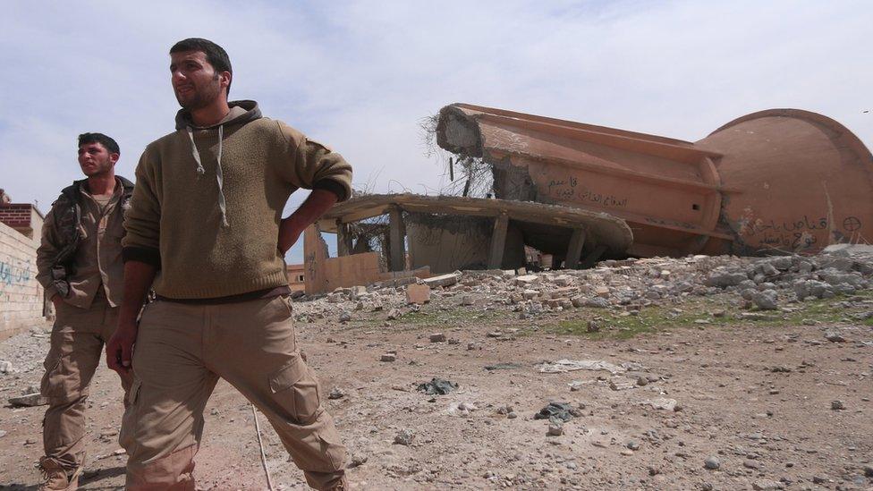 Syrian Democratic Forces fighters walk among damaged buildings to the east of Raqqa