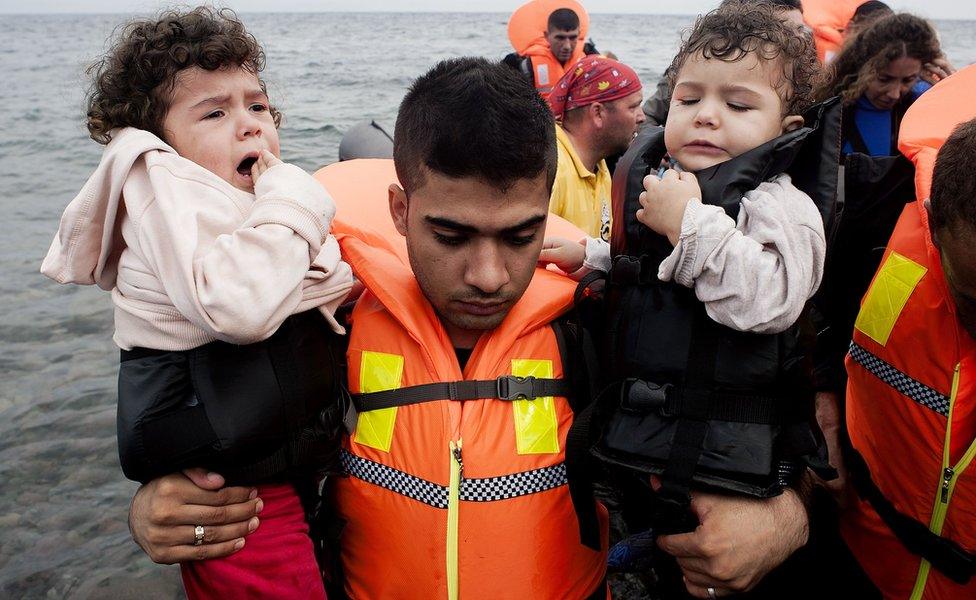 A refugee man carries children upon their arrival on Sykamia beach, west of the port of Mytilene, on the Greek island of Lesbos after crossing the Aegean sea from Turkey on September 22, 2015.