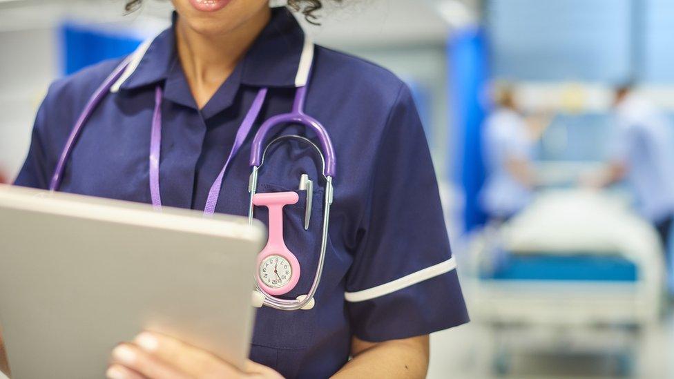 A nurse holding a tablet computer with a hospital ward in the background